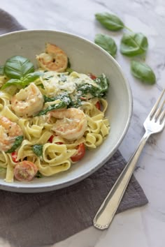 a white bowl filled with pasta and shrimp on top of a table next to silverware