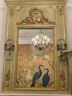 an ornate gold framed mirror with two birds on it and a chandelier hanging from the ceiling