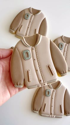 three cookies shaped like baby clothes being held by a person's hand on a white surface