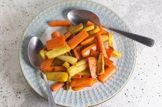 a plate full of carrots and potatoes with two spoons on the side next to it