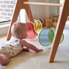 a baby laying on the ground next to a wooden frame with circles hanging from it