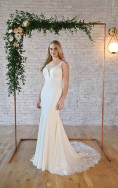 a woman standing in front of a white brick wall wearing a wedding dress with an open back