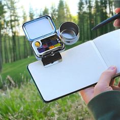 a person holding a camera and writing on a notepad with an open notebook in front of them