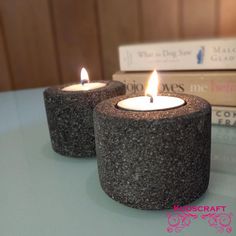 two lit candles sitting on top of a table next to some books and a cup