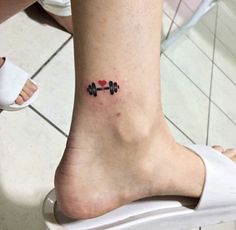 a small tattoo on the foot of a woman's leg with dumbbells