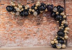 black and gold balloons are arranged in the shape of a heart on a brick wall