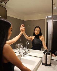 a woman is standing in front of a bathroom mirror holding her hand up to the sink