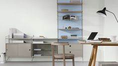 a desk with a laptop, bookshelf and lamp in an office space that has white walls