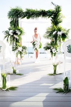 a woman is walking down the aisle with flowers and greenery