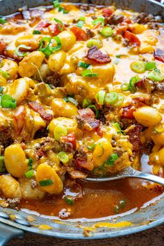 a large skillet filled with some taco meat and cheese covered in sauce, garnished with green onions