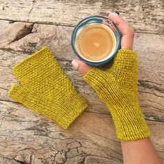 a person's hand holding a cup of coffee with yellow knitted mitts