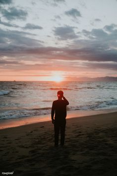 a man standing on top of a sandy beach next to the ocean under a cloudy sky