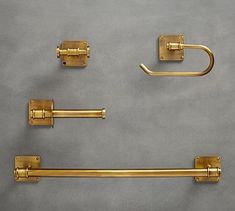 four brass bathroom accessories on a gray surface, including two towel bars and one toilet paper holder