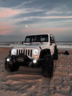 a white jeep parked on top of a sandy beach next to the ocean at sunset