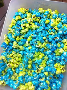 a plastic container filled with blue and green popcorn kernels on top of a table