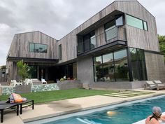 a woman sitting on the edge of a swimming pool in front of a large house