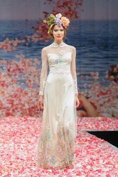 a woman walking down a runway wearing a white dress with flowers on it's head