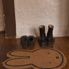 a pair of black boots sitting on top of a wooden floor next to a door mat