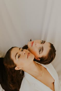 two women laying on top of each other in white clothing and one is holding her head up