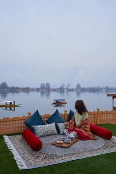 a woman sitting on top of a large rug in front of a body of water