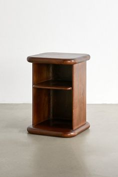 a small wooden shelf sitting on top of a cement floor next to a white wall