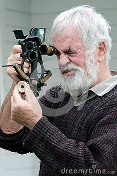 an old man holding a camera and looking at the viewer's eye with his hand