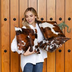 a woman holding two pillows in front of a wooden wall with an animal print pattern