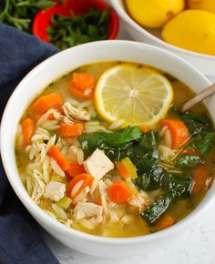 a bowl of chicken noodle soup with lemons, carrots and spinach