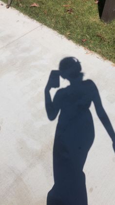 a shadow of a person on the sidewalk with a cell phone to their ear and hand in his other hand