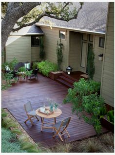 a wooden deck in front of a house surrounded by trees and bushes with chairs around it