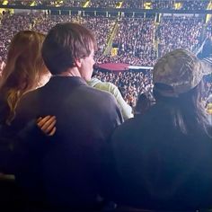 two people sitting in front of a large crowd at a sporting event, with one person holding his arms around the other