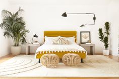 a bedroom with white walls and wooden flooring has a yellow bed, two planters on either side of the bed