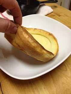 a person is dipping something into a bowl on a white plate with a wooden table in the background