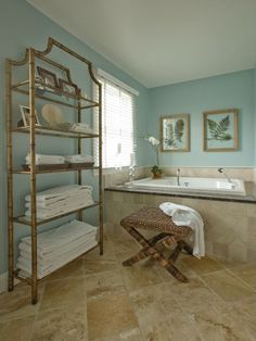 a bathroom with blue walls and tile flooring has a gold shelving unit next to the bathtub