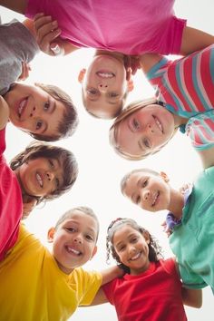 a group of children standing in a circle looking up at the camera with their hands together