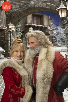 a man and woman dressed as santa claus in front of a snow - covered building