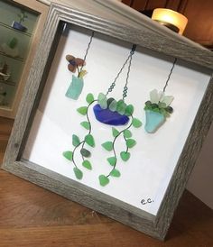 three vases with flowers are hanging in a frame on the table next to a candle