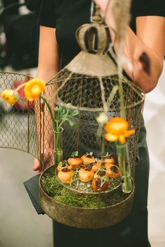 a person holding a birdcage with flowers in it and moss on the ground