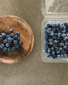 a wooden bowl filled with blueberries next to a plastic container full of blueberries