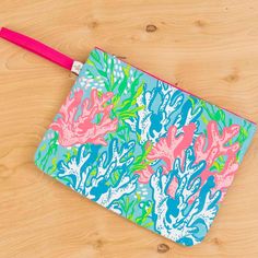 a blue and pink pouch with corals on it sitting on a wooden surface next to a red toothbrush