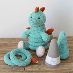 a blue crocheted dragon sits next to an orange and white object on a wooden table