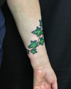 a woman's arm with green leaves on it and the wrist is covered in tattoos