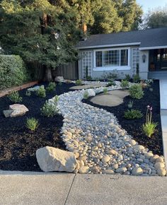 a house with rocks and plants in the front yard, along with a gravel path