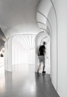 a man walking down a hallway next to a white building with arches and columns on the walls