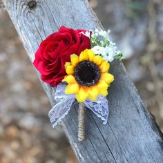 a sunflower and red rose boutonniere sitting on a wooden fence post