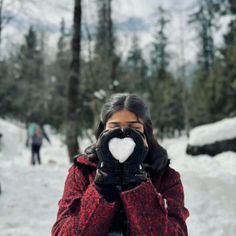 a woman in red jacket holding up a heart shaped object to her face while standing on snow covered ground