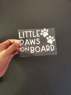 a hand holding a sticker that says little paws on board