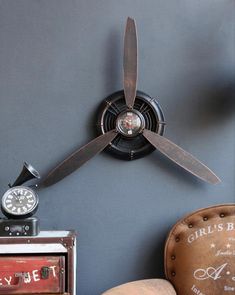 a ceiling fan mounted to the side of a wall next to a chair and clock