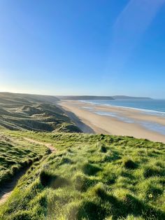 the sun shines brightly over an empty beach and grassy area near the water's edge