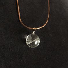 a necklace with a dandelion pendant hanging from it's side on a brown cord